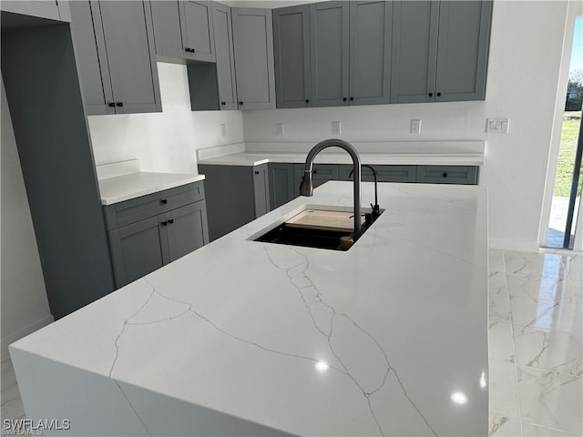 kitchen with light stone countertops, sink, and gray cabinetry