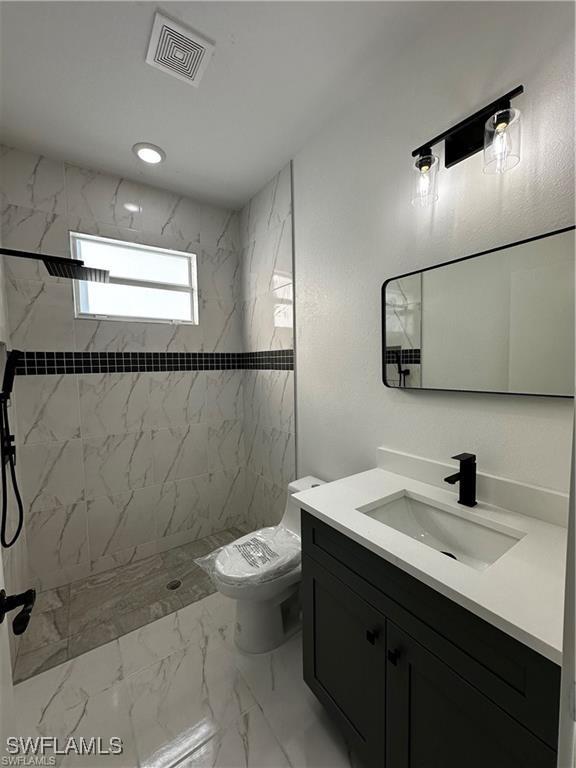 bathroom featuring vanity, tiled shower, and toilet