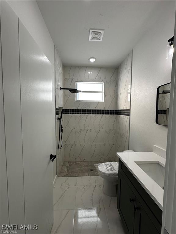 bathroom featuring vanity, toilet, and a tile shower