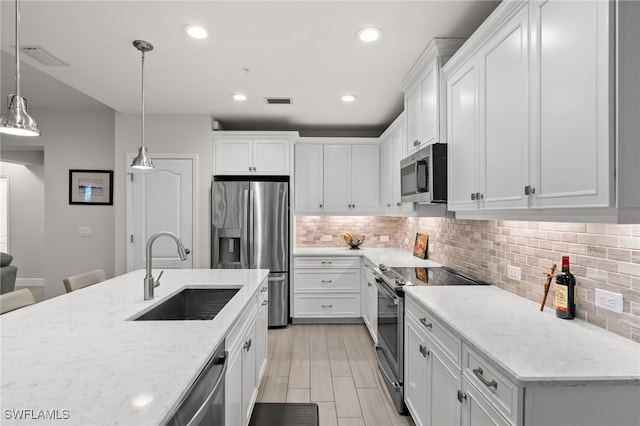 kitchen with sink, white cabinets, hanging light fixtures, stainless steel appliances, and light stone countertops