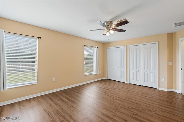 unfurnished bedroom featuring wood finished floors, two closets, visible vents, and baseboards