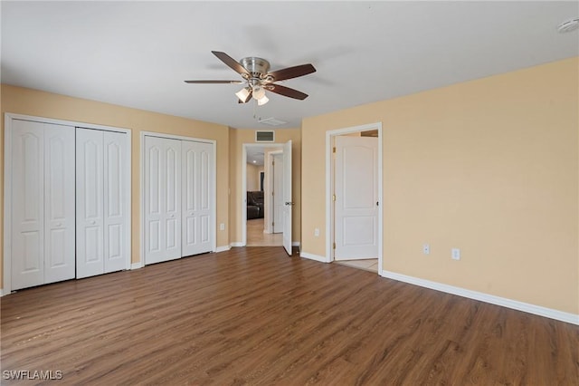 unfurnished bedroom featuring ceiling fan, wood finished floors, visible vents, baseboards, and two closets