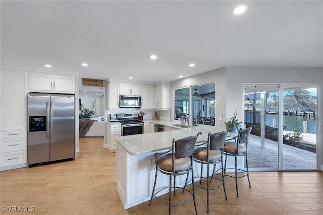 kitchen featuring sink, a water view, appliances with stainless steel finishes, light stone countertops, and white cabinets