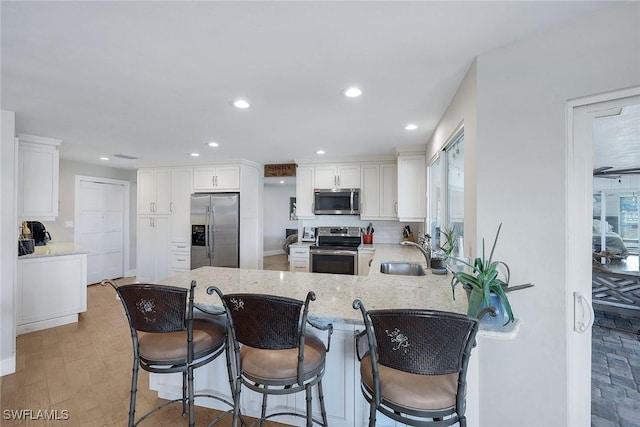 kitchen featuring appliances with stainless steel finishes, sink, white cabinets, a kitchen bar, and kitchen peninsula