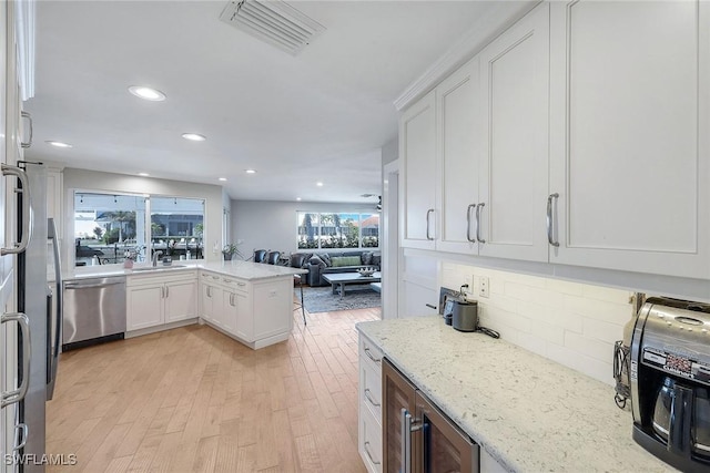 kitchen featuring white cabinetry, backsplash, stainless steel dishwasher, light hardwood / wood-style floors, and light stone countertops