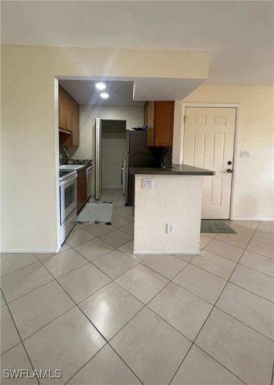 kitchen with black fridge, kitchen peninsula, light tile patterned floors, and electric stove