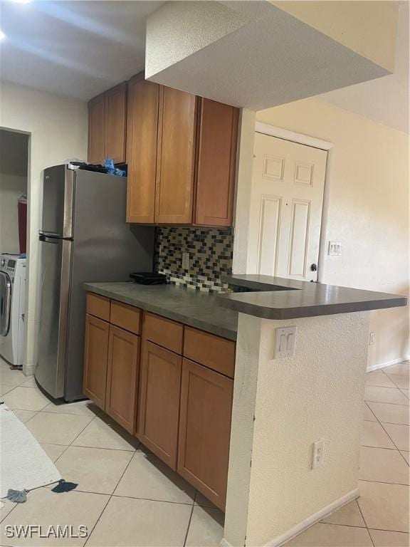 kitchen featuring light tile patterned flooring, stainless steel refrigerator, backsplash, kitchen peninsula, and washer and clothes dryer