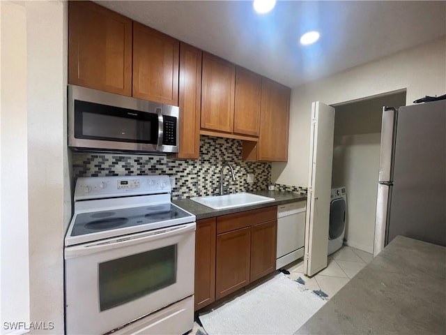 kitchen with sink, light tile patterned floors, appliances with stainless steel finishes, tasteful backsplash, and washer / clothes dryer