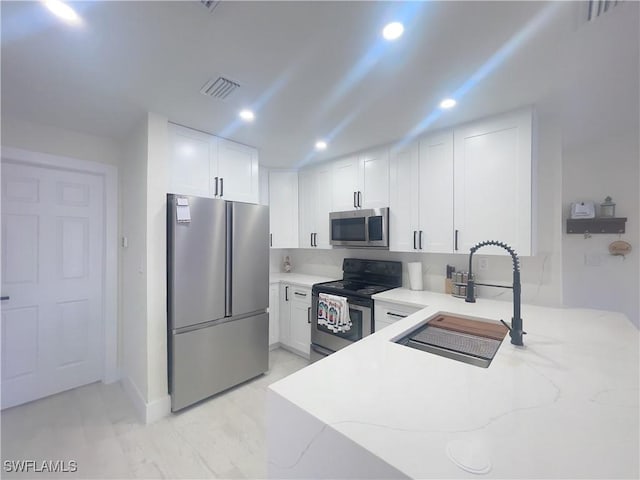 kitchen featuring sink, stainless steel appliances, light stone counters, white cabinets, and kitchen peninsula