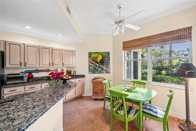 kitchen with light tile patterned floors, crown molding, a wealth of natural light, and dark stone counters