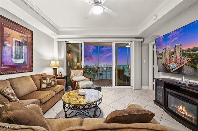 living area featuring a ceiling fan, a glass covered fireplace, crown molding, and light tile patterned floors