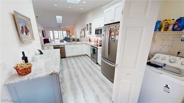 kitchen with appliances with stainless steel finishes, white cabinetry, light stone countertops, washer / clothes dryer, and kitchen peninsula