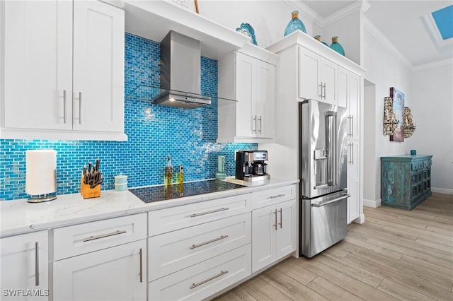 kitchen featuring wall chimney range hood, high end refrigerator, white cabinets, and black electric cooktop