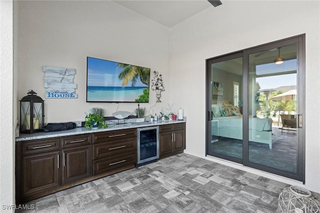 bar featuring dark brown cabinetry, light stone countertops, and beverage cooler