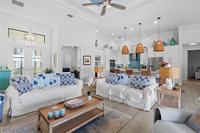 living room with a towering ceiling, ceiling fan with notable chandelier, french doors, ornamental molding, and light hardwood / wood-style flooring