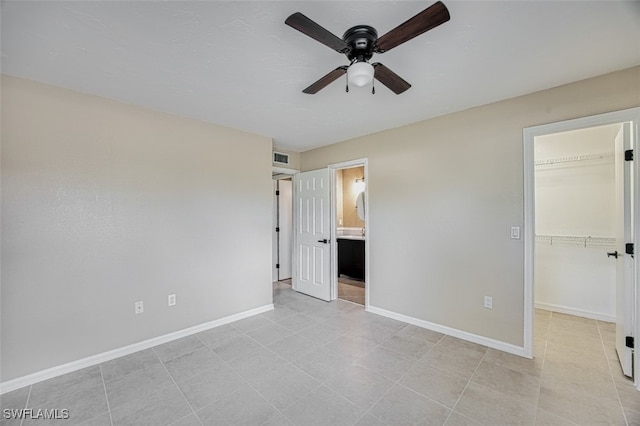 unfurnished bedroom with a spacious closet, ensuite bath, a closet, and ceiling fan