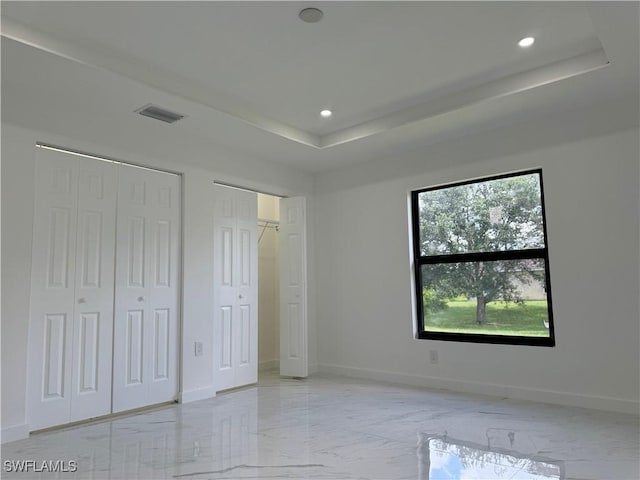 unfurnished bedroom with multiple closets and a tray ceiling