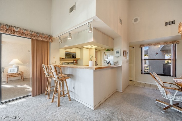 kitchen featuring a towering ceiling, a breakfast bar area, light colored carpet, and kitchen peninsula