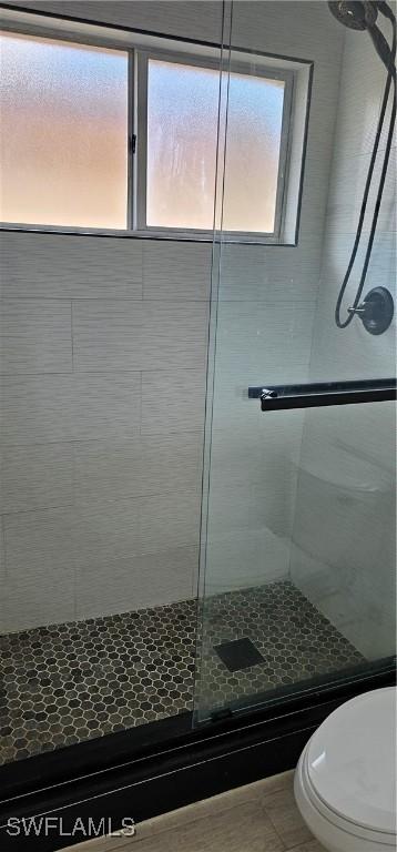 bathroom featuring a shower with door and toilet