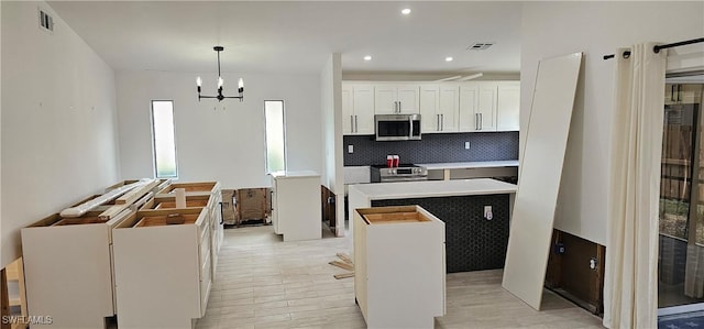 kitchen with appliances with stainless steel finishes, white cabinetry, a center island, tasteful backsplash, and decorative light fixtures