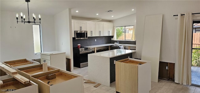 kitchen with pendant lighting, appliances with stainless steel finishes, white cabinetry, a center island, and tasteful backsplash