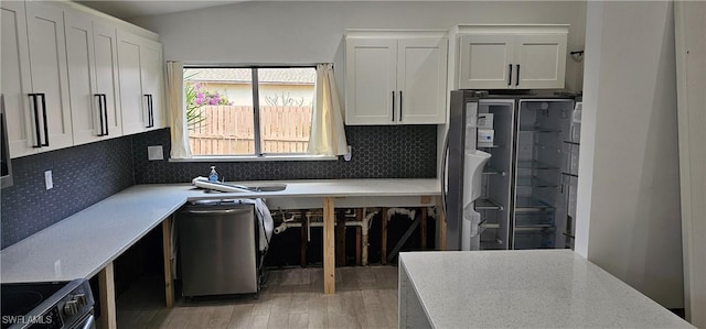 kitchen with appliances with stainless steel finishes, tasteful backsplash, sink, white cabinets, and hardwood / wood-style flooring