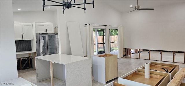 kitchen with light hardwood / wood-style flooring, stainless steel fridge, high vaulted ceiling, white cabinets, and a kitchen island