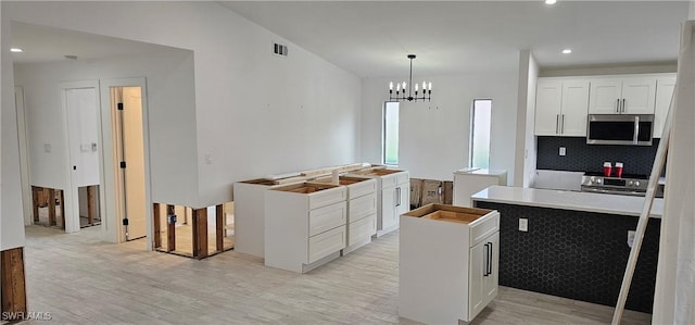 kitchen featuring appliances with stainless steel finishes, white cabinetry, a kitchen island, decorative light fixtures, and light wood-type flooring