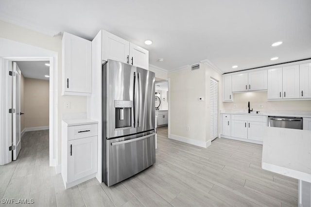 kitchen with appliances with stainless steel finishes, sink, white cabinets, crown molding, and light stone countertops