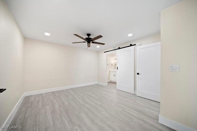 unfurnished bedroom with ceiling fan, ensuite bathroom, a barn door, and light hardwood / wood-style flooring