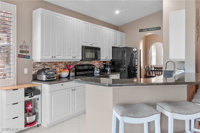 kitchen with arched walkways, a breakfast bar area, a peninsula, white cabinetry, and black appliances