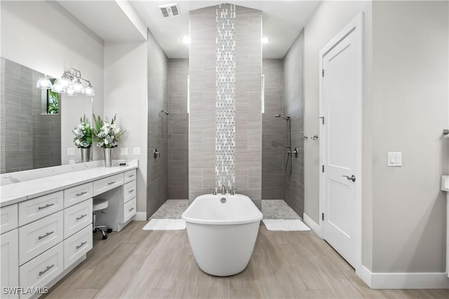 full bathroom with vanity, a walk in shower, visible vents, and a freestanding bath
