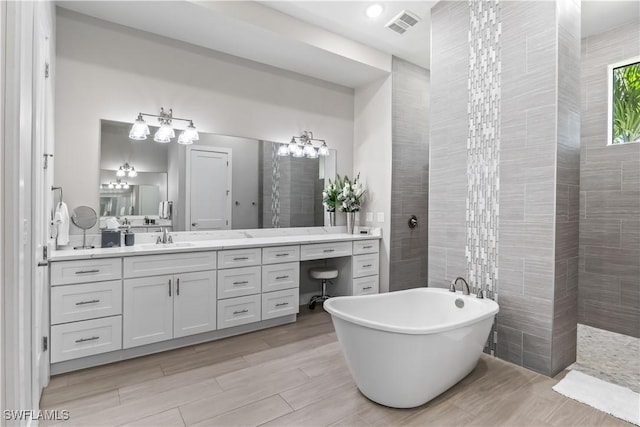 full bathroom featuring vanity, visible vents, a soaking tub, tile walls, and a chandelier
