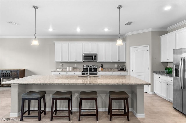 kitchen with decorative light fixtures, stainless steel appliances, a kitchen island with sink, and white cabinets