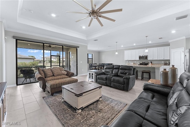 tiled living room with ceiling fan, a tray ceiling, ornamental molding, and sink