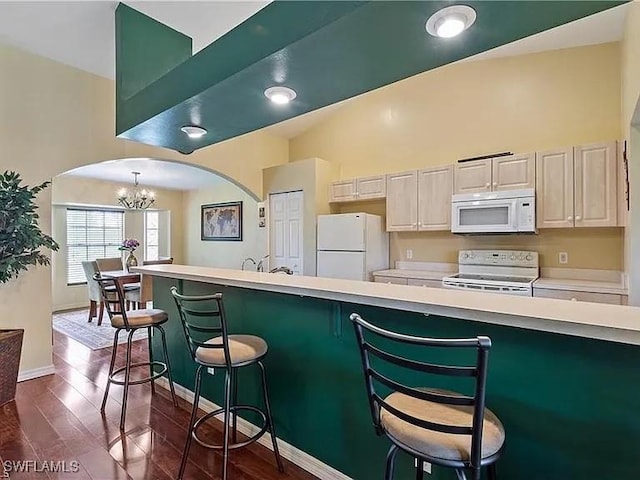 kitchen featuring a breakfast bar, decorative light fixtures, white appliances, dark wood-type flooring, and an inviting chandelier