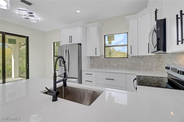 kitchen with tasteful backsplash, appliances with stainless steel finishes, sink, and white cabinets