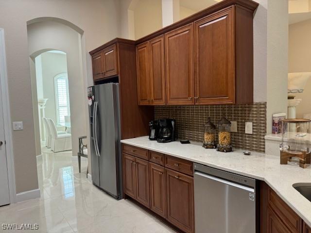 kitchen with stainless steel appliances, light stone countertops, and backsplash