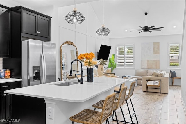 kitchen with hanging light fixtures, stainless steel fridge, a kitchen breakfast bar, and an island with sink