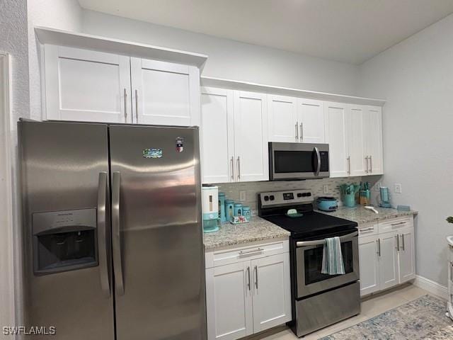 kitchen featuring appliances with stainless steel finishes, white cabinets, backsplash, and light stone countertops