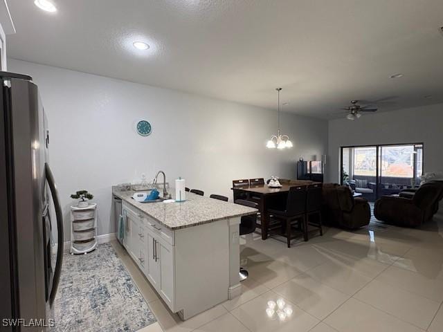 kitchen featuring a sink, white cabinets, open floor plan, freestanding refrigerator, and light stone countertops