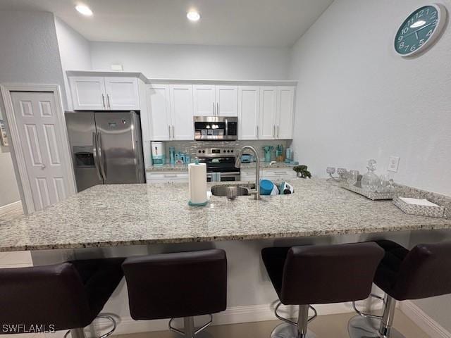 kitchen featuring appliances with stainless steel finishes, a breakfast bar, white cabinetry, and light stone countertops