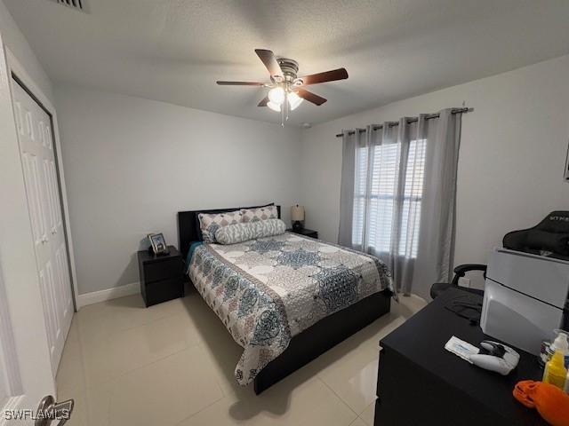 bedroom with baseboards, a ceiling fan, a closet, and light tile patterned flooring