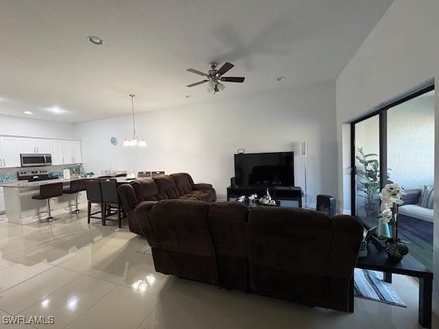 living area with light tile patterned floors, ceiling fan with notable chandelier, and recessed lighting