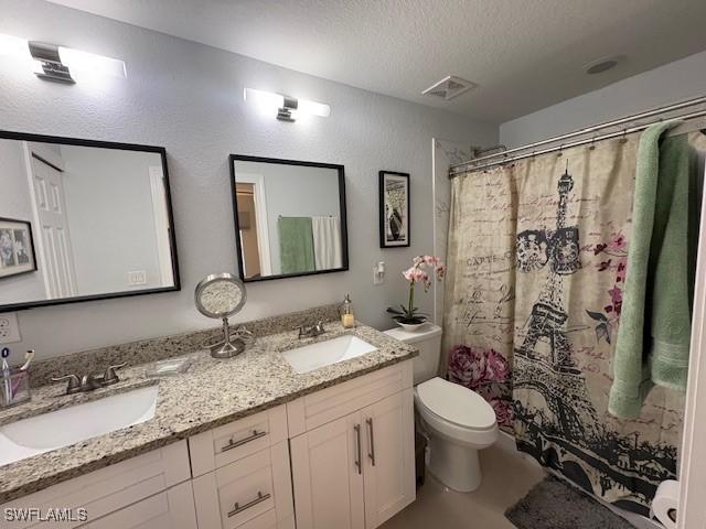 full bath with a sink, a textured ceiling, toilet, and double vanity