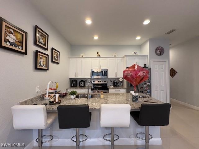 kitchen with appliances with stainless steel finishes, a breakfast bar, a sink, and white cabinetry