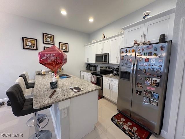 kitchen featuring appliances with stainless steel finishes, a kitchen bar, light stone countertops, and white cabinets