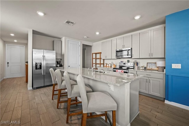 kitchen featuring appliances with stainless steel finishes, a kitchen bar, light hardwood / wood-style floors, and an island with sink