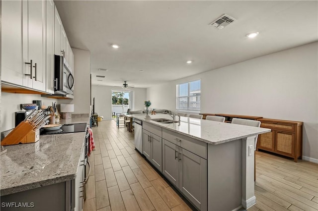 kitchen featuring stainless steel appliances, light stone countertops, a kitchen island with sink, and sink