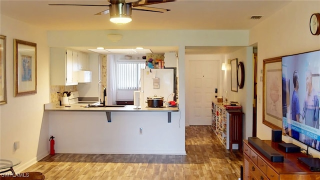 kitchen with a breakfast bar area, light hardwood / wood-style flooring, white cabinetry, kitchen peninsula, and white fridge